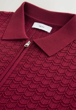 Viininpunainen neulottu poolopaita, jossa on teksturoitu aallokuvio, puoli vetoketjua edessä ja resorikaulus. Labelissa lukee "NEXT".