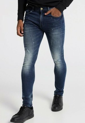 Skinny-fit denim jeans in dark blue with fading and distressed details, embellished with small white speckles, paired with black sneakers.
