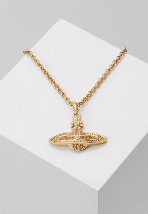 Gold chain necklace with a gold pendant shaped like a planet with rings and a bow detail on top, placed on a white block.