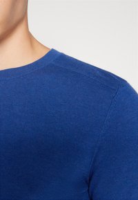 Maglione blu lavorato a maglia con scollo rotondo e texture a coste, caratterizzato da polsini e spalle lisce, che mette in evidenza un tessuto morbido.