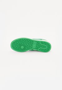 Grüne Gummi-Schuhsohle mit einem strukturierten Muster für besseren Halt, einer weißen Umrandung und einem kreisförmigen Akzent.