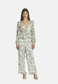 Bloemenjumper in zachte, lichte stof. Kenmerken zijn een diepe V-hals, lange mouwen, een peplum taille en wijde broekspijpen met groene en roze patronen.