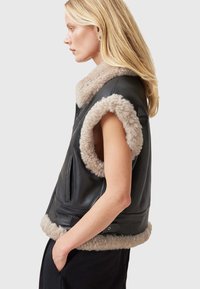 Must must vest, mille väikese beezist karusnahast krae ja käeavadega, lukuga esiosa ja kahe esikoti abil. Sile tekstuur.