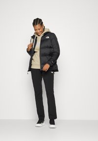 Black puffer jacket with a shiny texture, paired with a beige hoodie and black pants. The outfit features a logo on the jacket and hoodie.