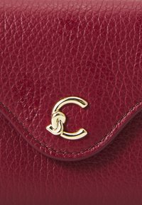 Deep red leather clutch with textured finish, featuring a gold metal logo accent and a curved flap closure.