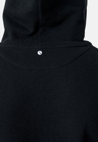 Melnas kapuces apģērba aizmugures skats ar nelielu baltu apļveida logotipu, kas centrēts zem kapuces šuves.