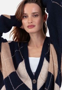 Cardigan en tricot présentant un motif losanges bleu marine et beige, encolure en V, manches amples et boutons à l'avant. Tissu en mélange de laine texturé.