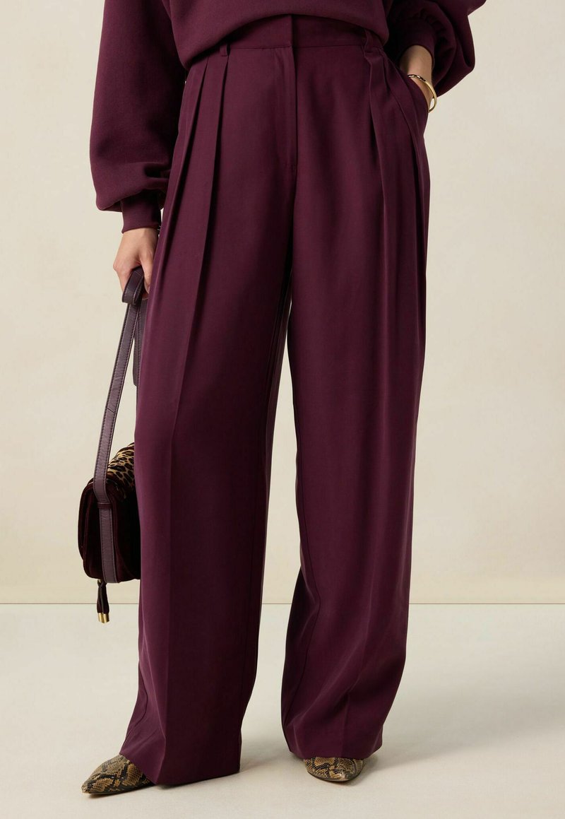 Vrouw in hoge taille, wijde pruimenbroek, met een handtas van luipaardprint en met puntige schoenen met een slangpatroon.