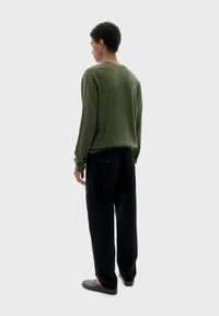 Zelený pletený svetr s kulatým výstřihem, spárovaný s širokými černými kalhotami. Textura je měkká a outfit má minimální kovové detaily.