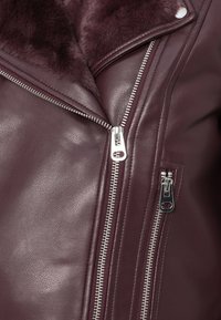 Burgundská kožená bunda se syntetickým kožešinovým límcem, asymetrickým zipem a stříbrnými detaily. Hladká textura s elegantním designem.