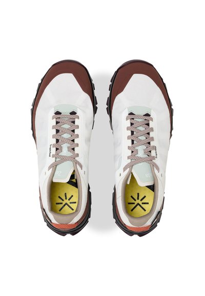 Une paire de baskets blanches avec des bouts et des semelles marron, des lacets gris clair et des semelles intérieures jaunes avec un motif d'étoiles noires, vue de dessus.