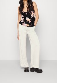 Débardeur noir à fleurs avec des fleurs roses et blanches, associé à un pantalon large beige clair et des chaussures compensées noires épaisses.
