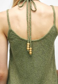 Débardeur en maille verte avec un large dos, des bretelles fines et des liens ajustables ornés de perles en bois pour le détail. Texture douce, design décontracté.