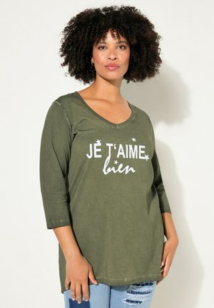 Tunique vert olive avec un décolleté arrondi et des manches 3/4, ornée du texte blanc "JE T'AIME bien" avec des accents d'étoiles. Tissu en mélange de coton doux.