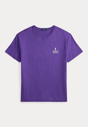 Camiseta de algodón púrpura con mangas cortas, cuello redondo y un pequeño logo blanco de Polo en el pecho izquierdo. Textura de tela suave.