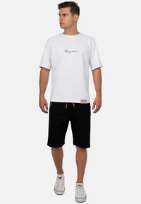 Witte t-shirt met korte mouwen en een zwart logo, gecombineerd met zwarte shorts en witte sneakers. Casual, ontspannen pasvorm met ronde hals.