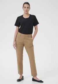 T-shirt en coton noir associé à un chino beige à coupe droite, avec poches avant et une texture lisse. Des ballerines noires complètent la tenue.