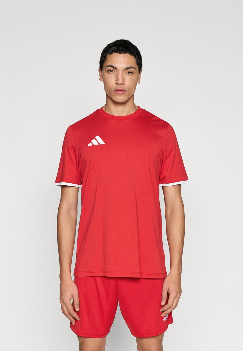 Κόκκινο αθλητικό μπλουζάκι με λευκές λεπτομέρειες και στρογγυλή λαιμόκοψη, κατασκευασμένο από ελαφρύ ύφασμα. Φέρει το λογότυπο με τρεις λευκές ρίγες στο αριστερό μέρος του στήθους.