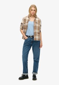 Geruite flanellen overhemd in beige en crèmekleurig, blauwe tanktop, blauwe spijkerbroek en zwarte schoenen met een ronde neus. Casual fit met opgerolde mouwen.