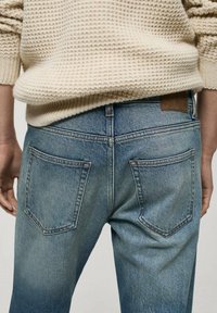 Jeans din denim de culoare albastră deschisă, cu un finisaj decolorat, având două buzunare la spate și o etichetă din piele maro pe talie.