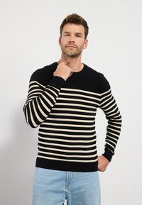 Suéter de punto a rayas negras y crema con textura acanalada y cuello redondo. Presenta mangas largas y un dobladillo negro ajustado.
