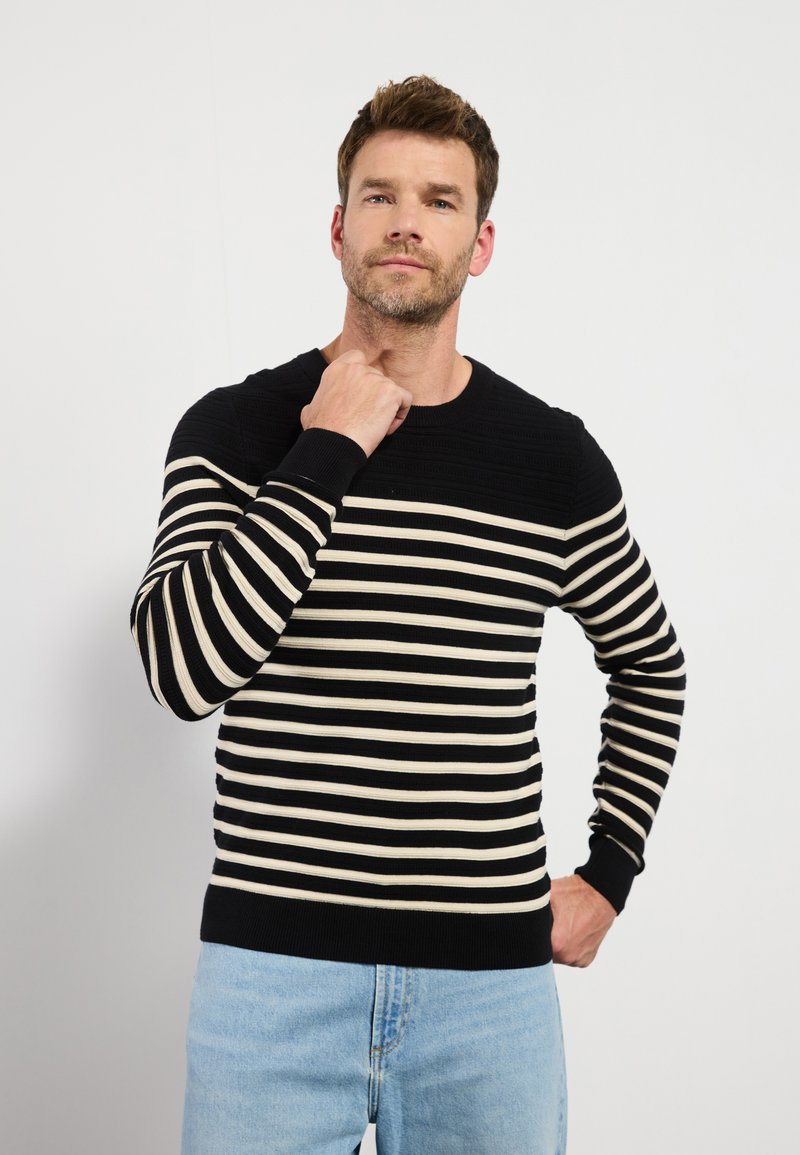 Suéter de punto a rayas negras y crema con textura acanalada y cuello redondo. Presenta mangas largas y un dobladillo negro ajustado.