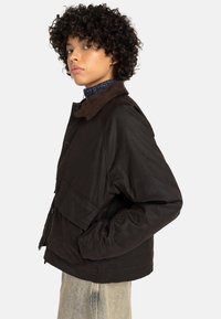 Veste noire avec un col en velours côtelé, dotée de poches avant et d'une coupe décontractée. La texture semble lisse avec un design durable.