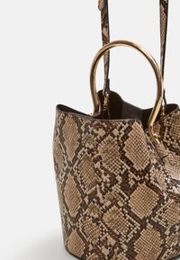 Sac fourre-tout à motif peau de serpent en beige et marron, avec une texture lisse et des ferrures dorées. Il présente une forme structurée et des poignées doubles.