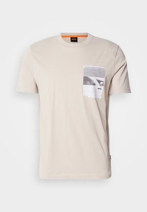 Beige cotton T-shirt with a crew neck and short sleeves. Features a front pocket with a black and white graphic print and logo.