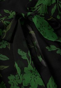 Tissu noir à surface texturée avec imprimé floral vert noué en un nœud lâche.