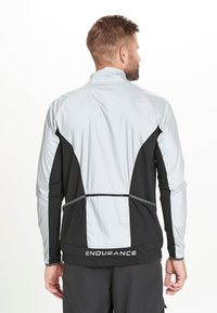 Letvægts atletisk jakke i grå og sort. Har en lynlåskrave, kontrasterende paneler og "ENDURANCE" logo ved kanten. Glat tekstur.