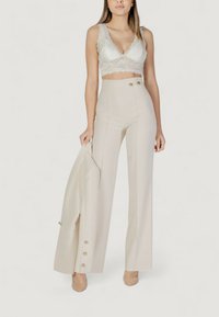 Bralette in pizzo di un crema chiaro con bordi scallop, abbinato a pantaloni beige a vita alta con due bottoni e design a gamba svasata.