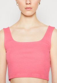 Vaaleanpunainen ribattu crop-top, jossa on neliskulmainen kaula-aukko ja leveät hihnat, valmistettu pehmeästä kankaasta. Sisältää siistit saumat ja istuvan siluetin.
