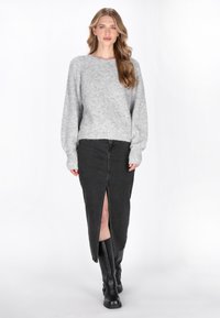 Pulover gri tricotat cu mâneci lungi, combinat cu o fustă din denim neagră cu o fanta frontală. Cizmele negre până la genunchi completează ținuta.