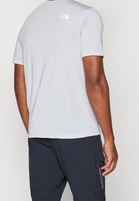 Ljusgrå kortärmad t-shirt med rund hals och liten vit logotyp på övre ryggen, tillverkad av mjukt, slätt tyg.