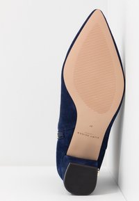 Mørkeblå ruskinds sko med spids tå, smal hæl og tekstureret sål. Har en lynlåsdetalje på siden. Størrelse 37.