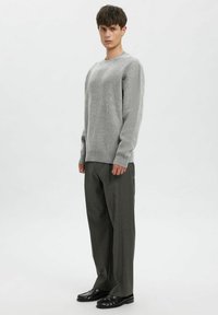 Grå strikket genser med lange ermer og rund hals; kombinert med løstsittende mørkegrå bukser og svarte sko. Enkel, teksturert design.