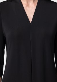 Top nero a scollo a V con maniche tre quarti, realizzato in un tessuto liscio e leggermente testurizzato, con una cucitura verticale al centro.