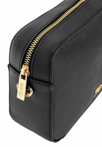 Czarna torebka o fakturowanej powierzchni z wyraźnym złotym zamkiem błyskawicznym, wyposażona w markowy uchwyt i prostą linię; prostokątny kształt z solidną konstrukcją.