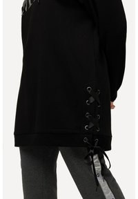 Schwarzes Sweatshirt mit seitlichem Schnürdetail aus schwarzen Bändern und Metallösen. Hat ein lässiges Design und eine weiche Textur.