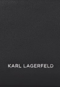 Portefeuille en cuir noir texturé présentant le logo "KARL LAGERFELD" en relief en blanc. Surface lisse avec un design minimaliste et des lignes épurées.