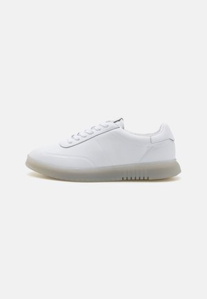 White athletic sneakers with a smooth leather upper, round toe, flat laces, and a translucent rubber sole featuring horizontal grooves.