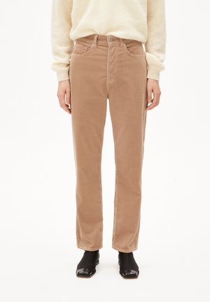 Beżowe spodnie sztruksowe o prostych nogawkach w połączeniu z kremowym swetrem i czarnymi botkami na kwadratowym nosku na białym tle.