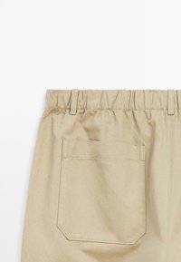 Pantalons beige avec taille élastique et poche arrière, dotés d'une coupe droite. Le tissu a une texture lisse et un léger fini brillant.