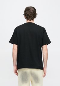 Camiseta de algodón negra con un corte holgado, mangas cortas y cuello redondo. Textura suave sin patrones ni detalles adicionales.