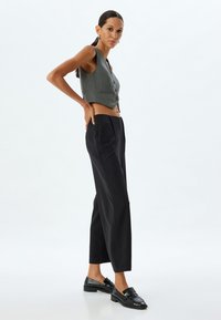 Grijze cropped vest met knopen, hooggeplaatste zwarte broek en zwarte loafers met gestructureerde details. Minimalistisch ontwerp en aansluitende silhoët.