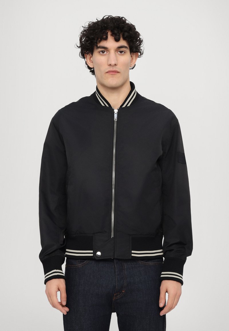 Giacca bomber nera con zip frontale, colletto e polsini a coste, con strisce bianche. Tessuto liscio e leggero; tasche laterali.