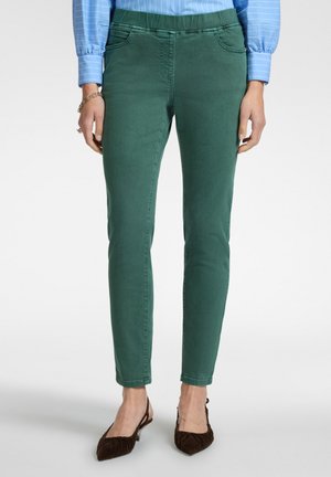 Pantalon slim vert avec poches avant, confectionné en tissu doux en mélange de coton. Ceinture élastique, associé à des ballerines pointues marron.