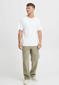 Weißes Baumwoll-T-Shirt mit kurzen Ärmeln, kombiniert mit hellolivgrünen Hosen. Das Outfit hat eine lockere Passform und weist minimalistische Designdetails auf.
