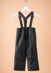 Pantalon imperméable noir avec bretelles ajustables, taille élastique et ourlets renforcés. Fabriqué en tissu léger et lisse, suspendu à un crochet blanc.